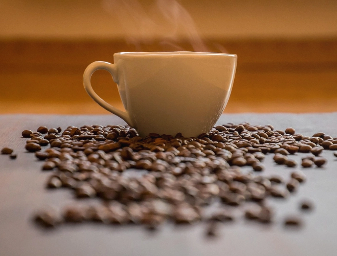 Hand gießt mit einem Milchkännchen ein Rosetta-Muster in einen Cappuccino